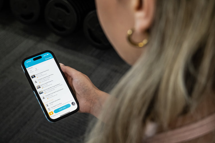 Person holding a smartphone with our online training plan open, while at the gym